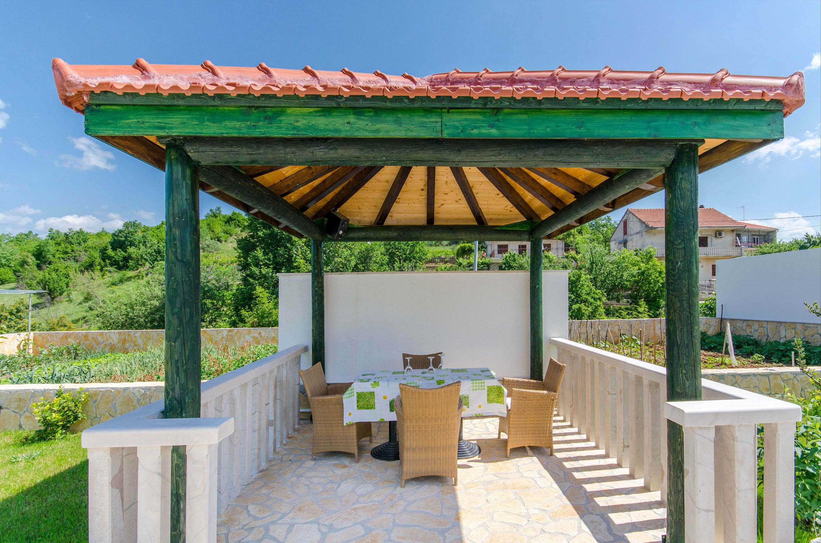 Un patio al aire libre con una mesa y sillas, una pérgola con techo de tejas y un piso de piedra.