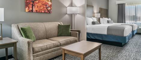 Une chambre d’hôtel avec un canapé, une petite table, un lit avec deux oreillers, une lampe et un tableau au mur.