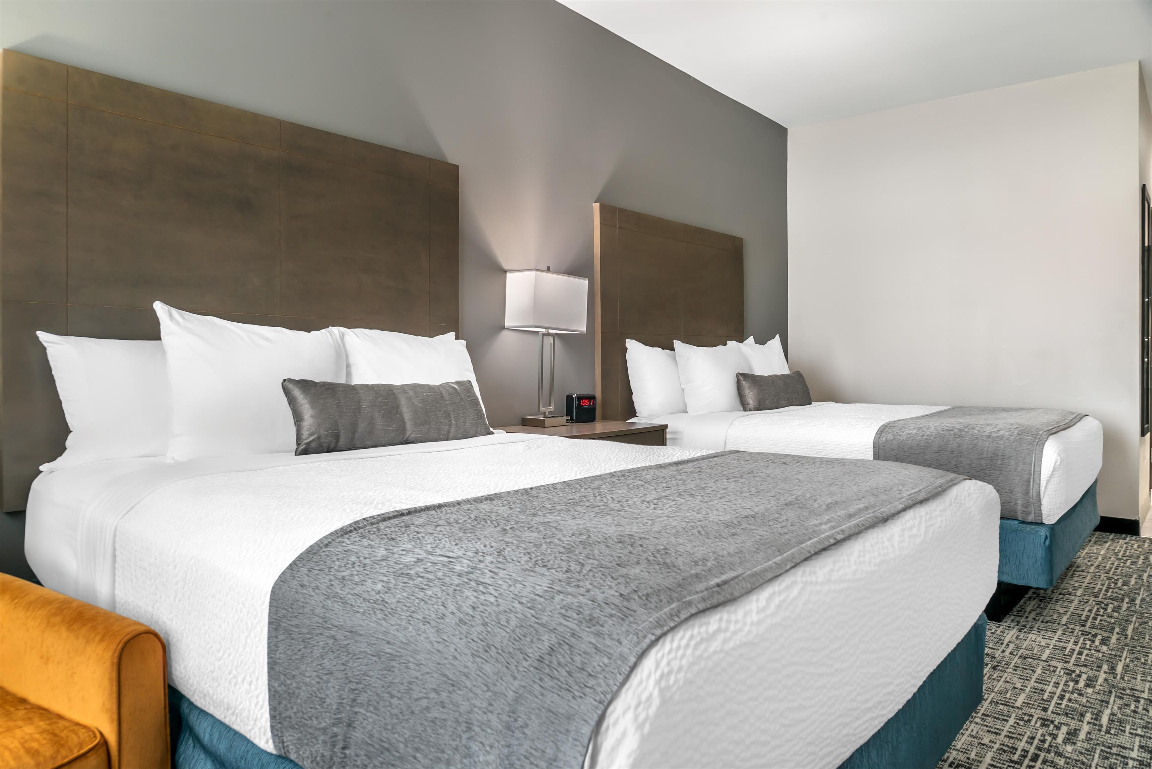 A hotel room with two beds, a nightstand, a lamp, and a clock.