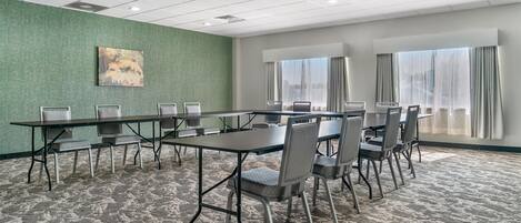 A conference room with a long table and chairs, a green textured wall, and large windows with curtains.