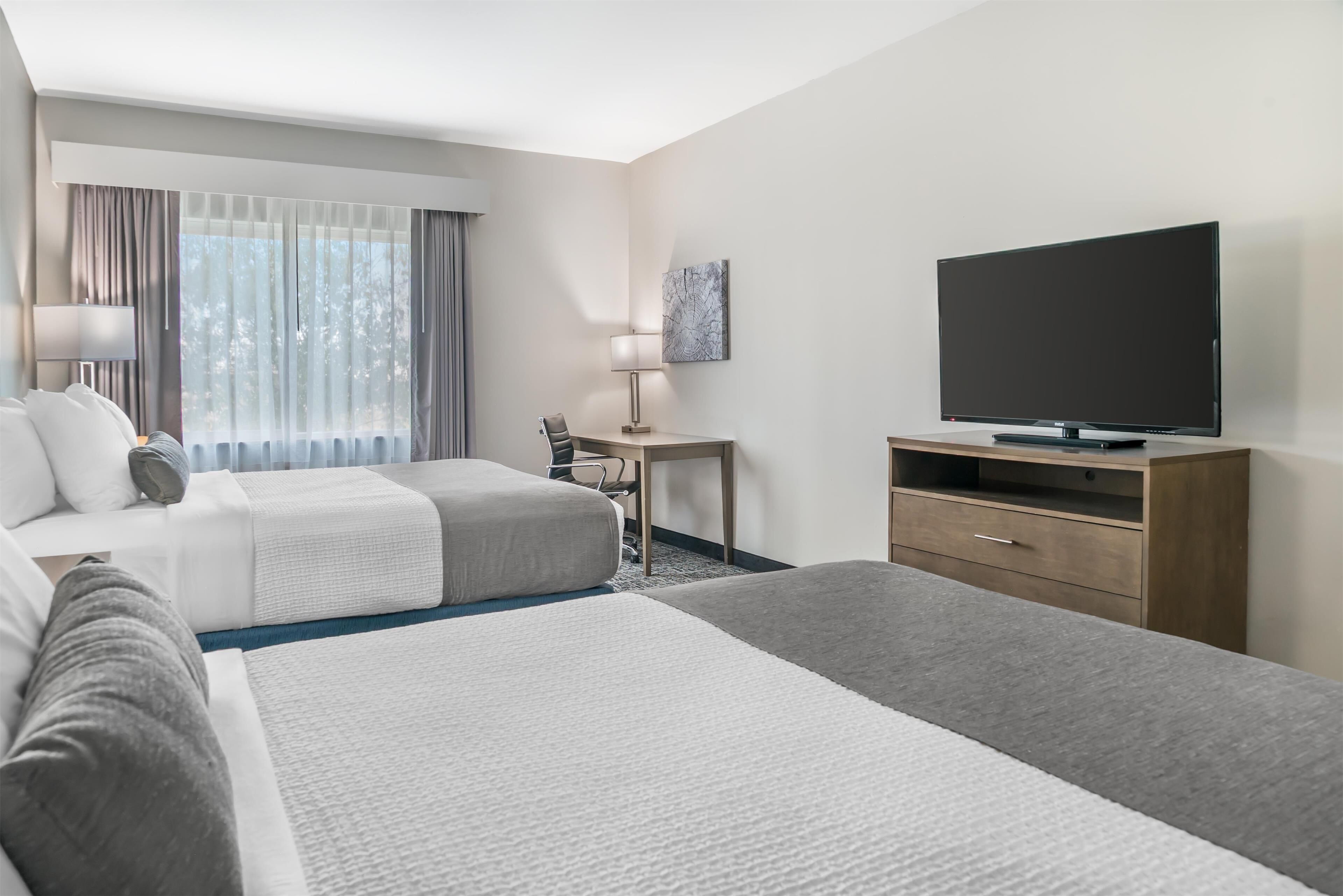 Habitación de hotel con dos camas, un escritorio, un televisor y una ventana con cortinas.