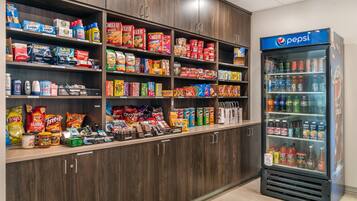 Una sección de aperitivos y bebidas con estantes llenos de diferentes opciones y un refrigerador de Pepsi.