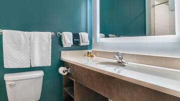 A bathroom with teal walls, a white toilet, a wooden vanity with a mirror, and two towels on the wall.