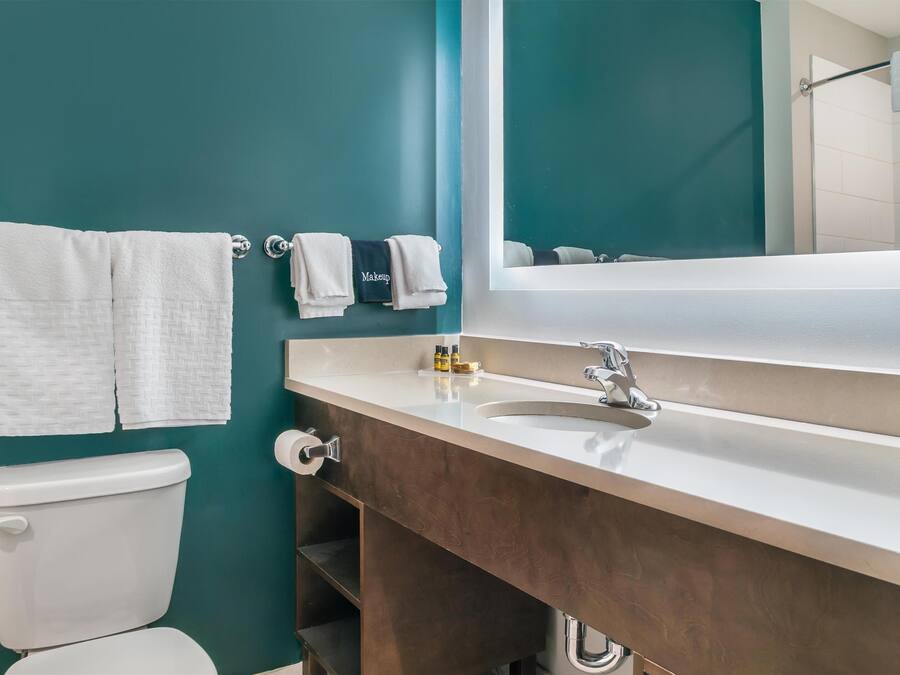 A bathroom with teal walls, a white toilet, a wooden vanity with a mirror, and two towels on the wall.