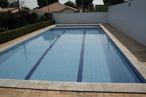 Una piscina rectangular con borde de azulejos y un trampolín.