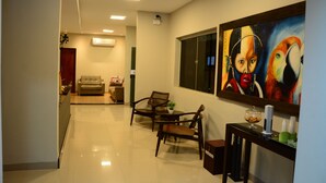 A modern living room with a sofa, two wooden chairs, a small table with a plant, and a painting on the wall. - Riviera Pantanal Hotel (Caceres)