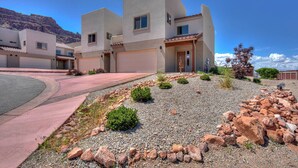 A modern two-story house with a driveway, a landscaped front yard with rocks and shrubs, and a mountain backdrop.