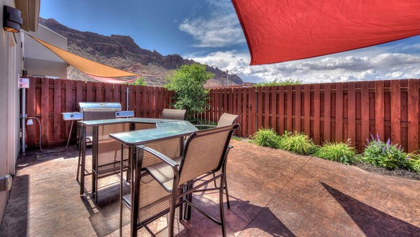 A patio with a grill, chairs, and a view of mountains.