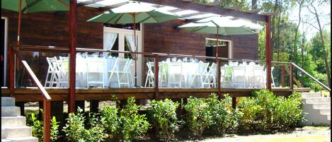 Terraza de madera con asientos al aire libre y sombrillas, rodeada de vegetación.