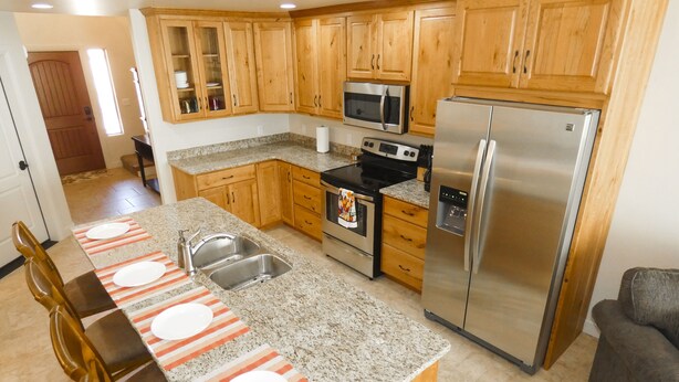 A kitchen with wooden cabinets, stainless steel appliances, a granite countertop, and a striped placemat. - Desert Winds 19 by MoabCondos4Rent (Moab)