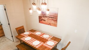 A dining area with a wooden table set for four, a rug, and a painting on the wall. - Desert Winds 19 by MoabCondos4Rent (Moab)
