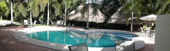 A swimming pool with lounge chairs and thatched umbrellas. - Green Jungle Hotel y Restaurante (Flores)