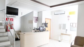 A reception area with a desk, computer, and a television mounted on the wall. There is a staircase with a fire extinguisher and a chair near the desk. - Hotel Borges (Quirinopolis)