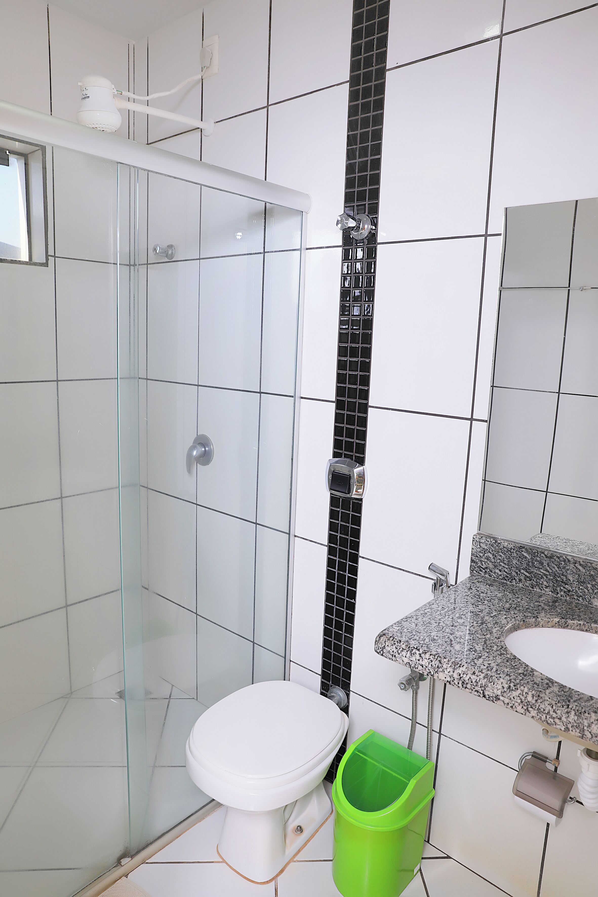 Bagno con doccia vetrata, water per il wc bianco, cestino verde e lavabo su piano in granito.