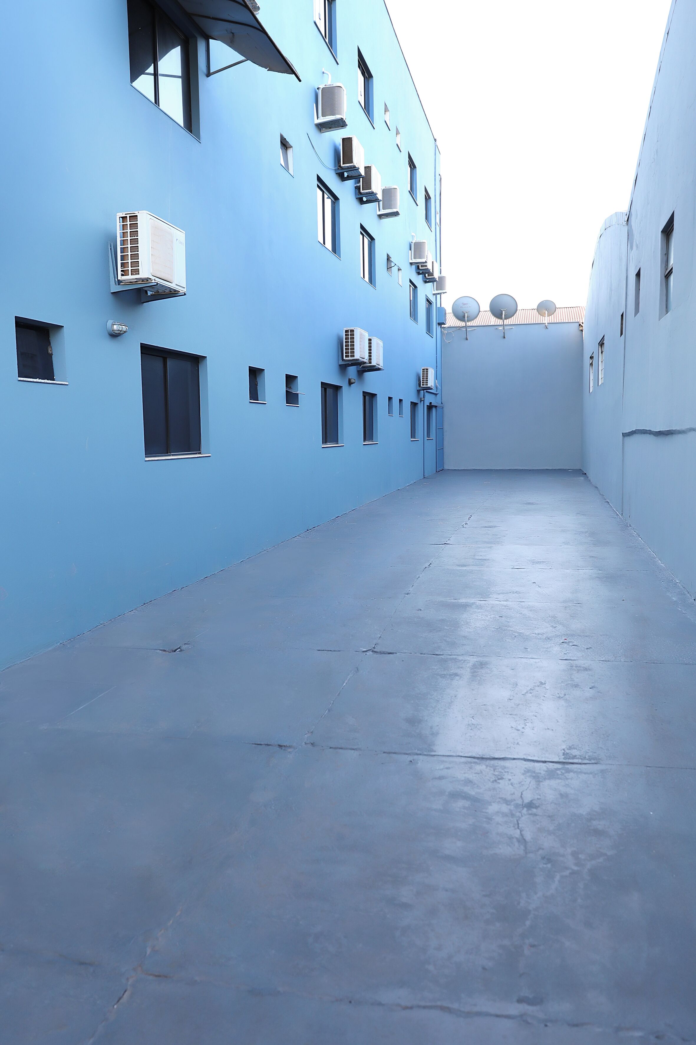 Ein schmaler Gang zwischen zwei Gebäuden mit blauen Wänden und mehreren an der Fassade befestigten Klimaanlagen.