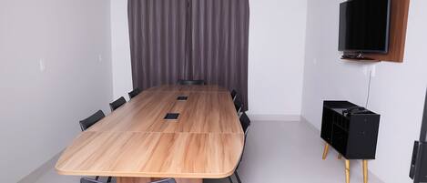 A conference room with a long wooden table, black chairs, a curtain, and a mounted TV.