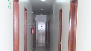 A long, narrow hallway with wooden doors on both sides, a fire extinguisher mounted on the wall, and a ceiling light fixture. - Hotel Borges (Quirinopolis)