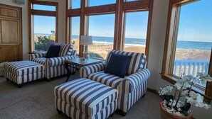 A room with large windows, striped upholstered sofas, a small table, and a potted plant. - Oceanfront, Heated Pool, Elevator, Book today! (Corolla)