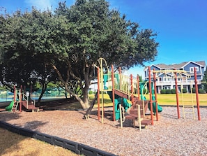 Um parquinho com diversas estruturas de recreação, cercado por árvores e um edifício ao fundo.