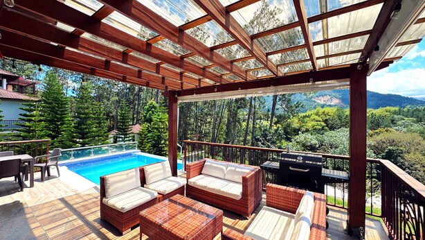 A covered outdoor area with a pool, wicker furniture, and a view of a forested landscape. - Vista del Campo Country Club & Villas (Jarabacoa)