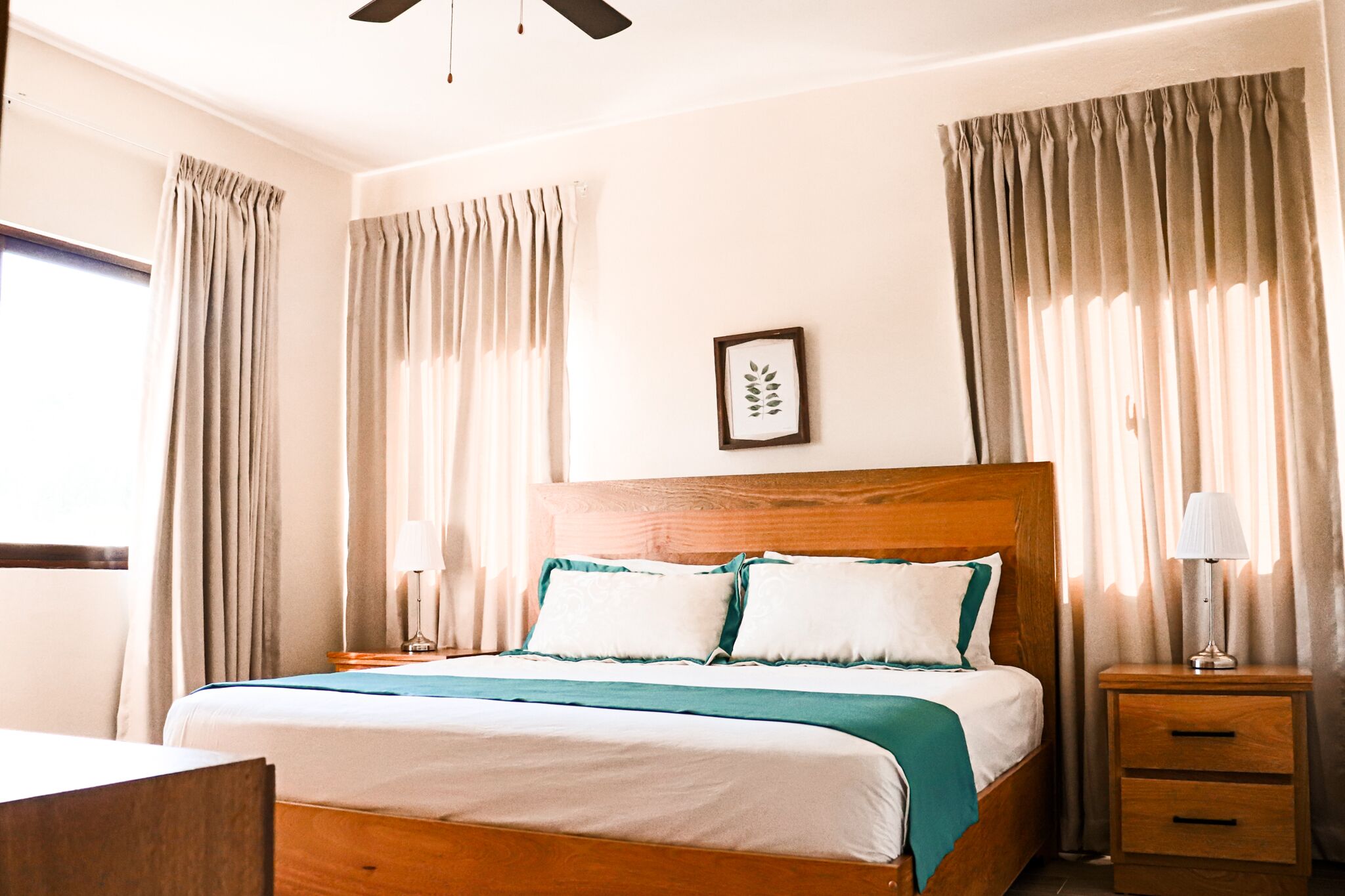 Ein Hotelzimmer mit einem hölzernen Bett, zwei Nachttischen, einem Deckenventilator und Vorhängen.