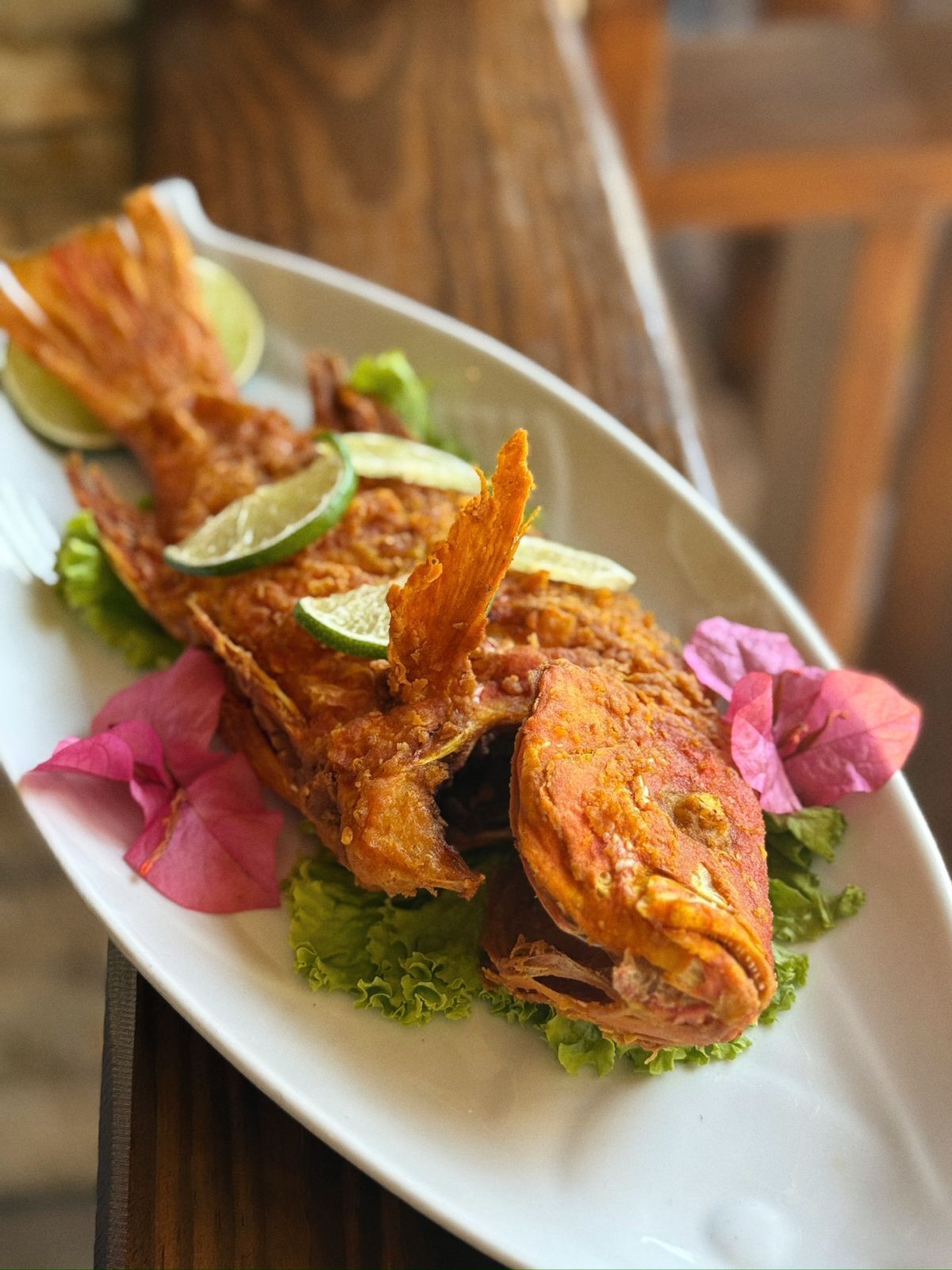 Un plato de pescado frito, adornado con rodajas de lima y flores rosadas.