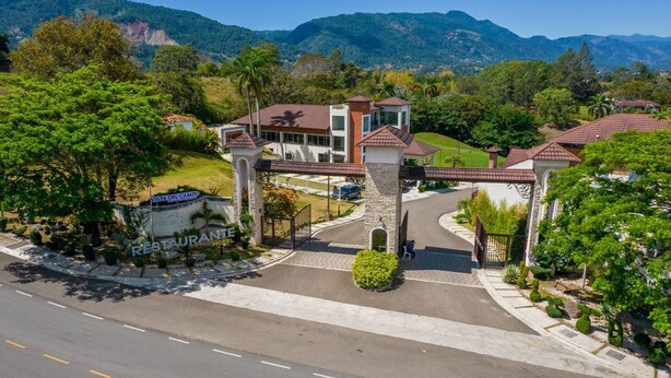 A hotel entrance with a stone archway, a sign for Vista Del Campo Restaurant, and a view of the surrounding greenery and mountains. - Vista del Campo Country Club & Villas (Jarabacoa)