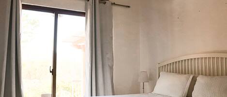 Une chambre à coucher avec un lit, une fenêtre avec des rideaux, un ventilateur de plafond et une chaise près de la fenêtre.