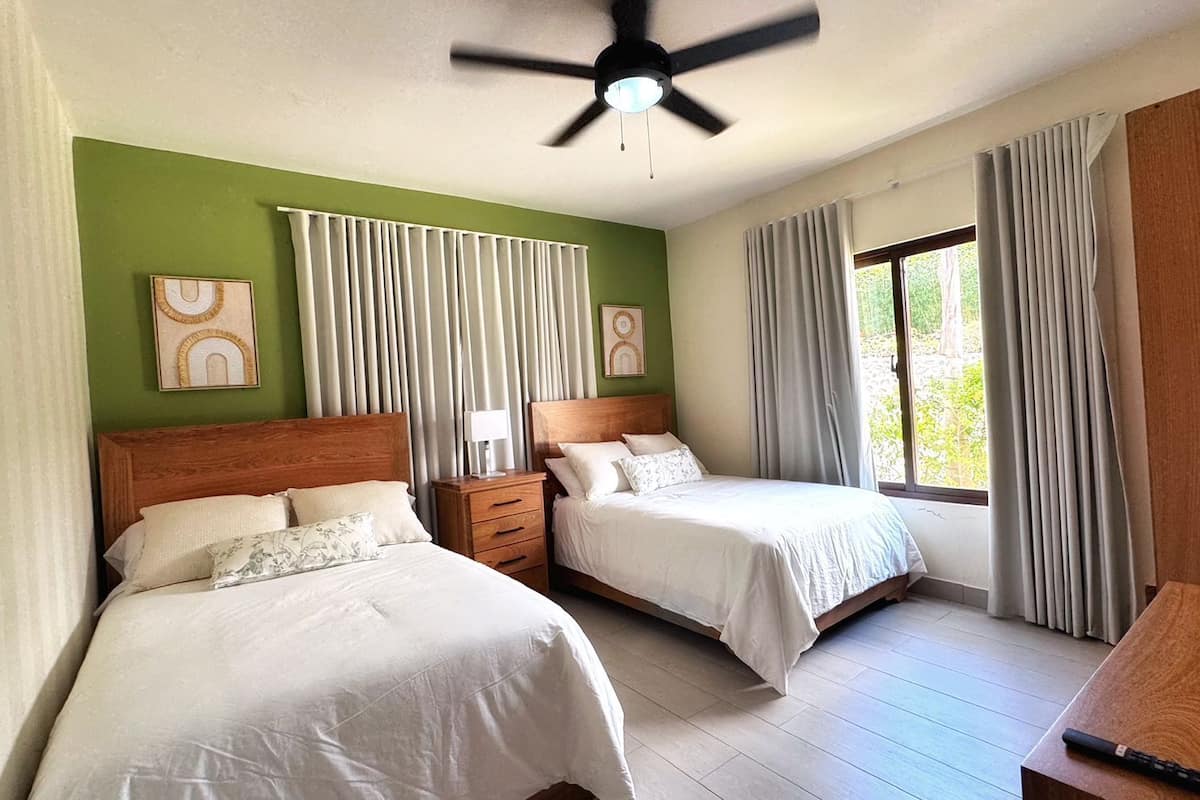 A hotel room with two beds, a ceiling fan, and a view of the outdoors.