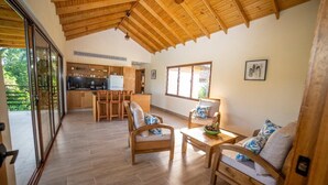 A spacious living area with wooden furniture, a kitchen in the background, and large windows. - Vista del Campo Country Club & Villas (Jarabacoa)