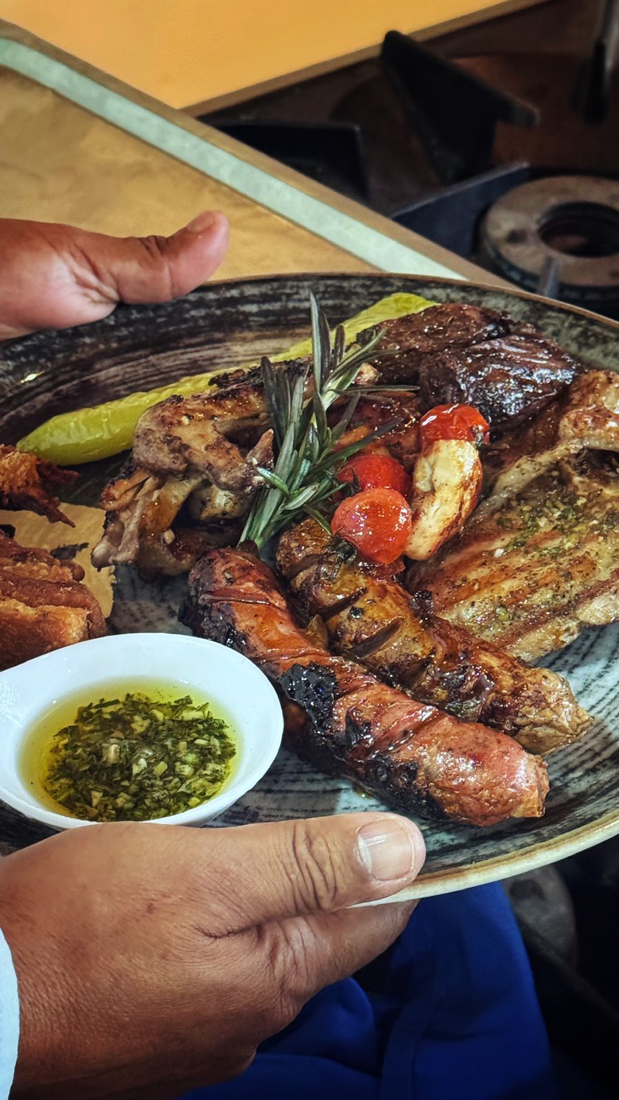 Una persona sosteniendo un plato con carne a la parrilla, verduras y un pequeño recipiente con salsa.