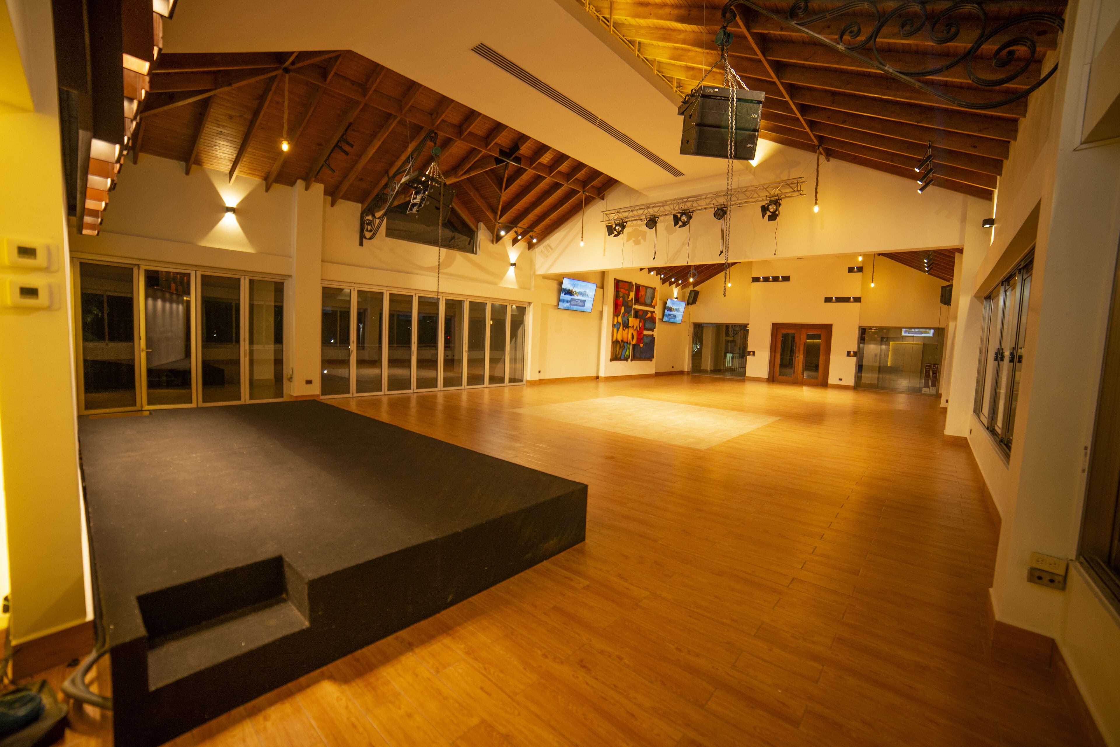 A spacious indoor area with wooden floors, a stage, and a high ceiling with exposed beams.
