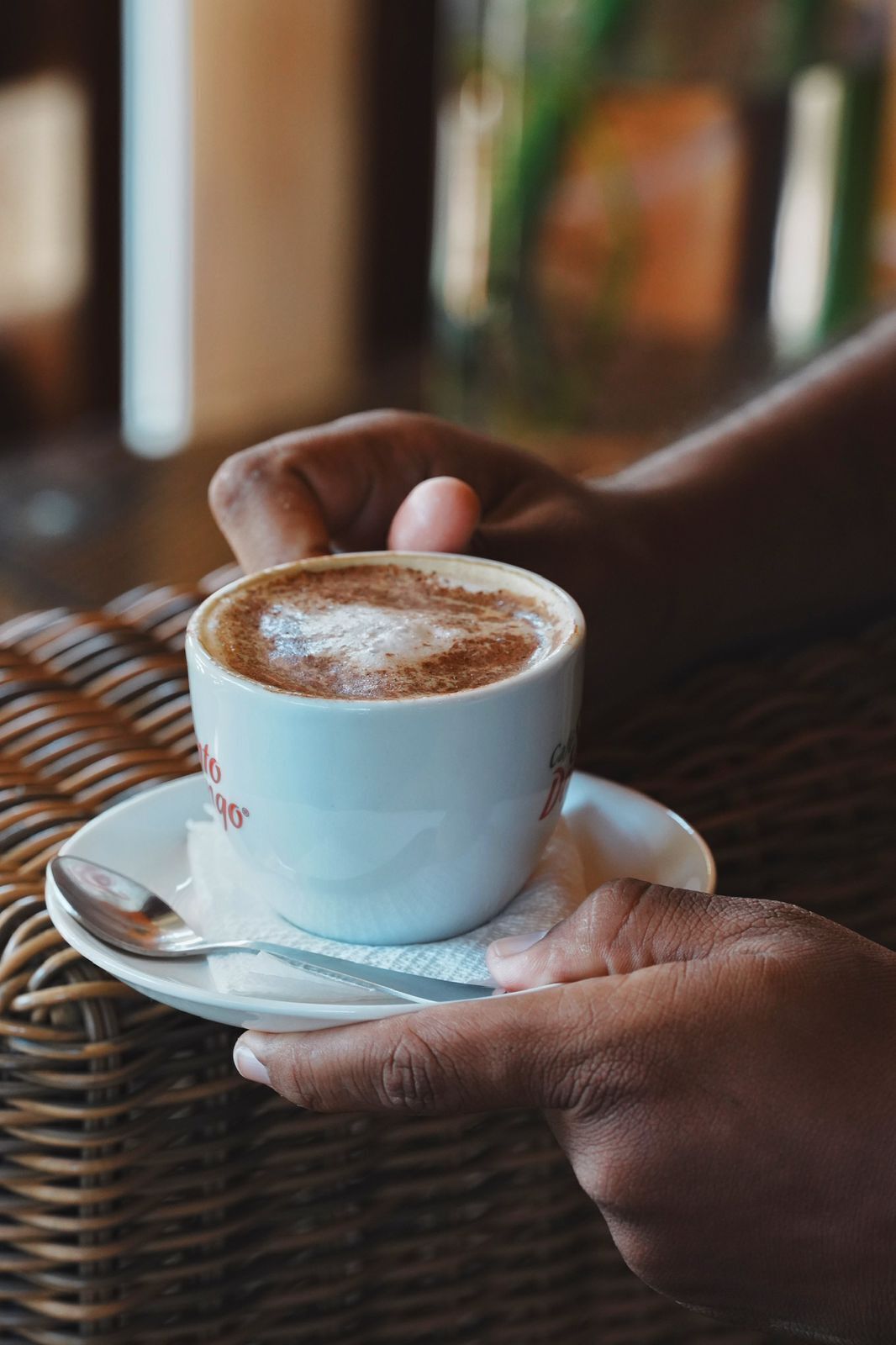 A cup of coffee on a saucer, held by a hand.