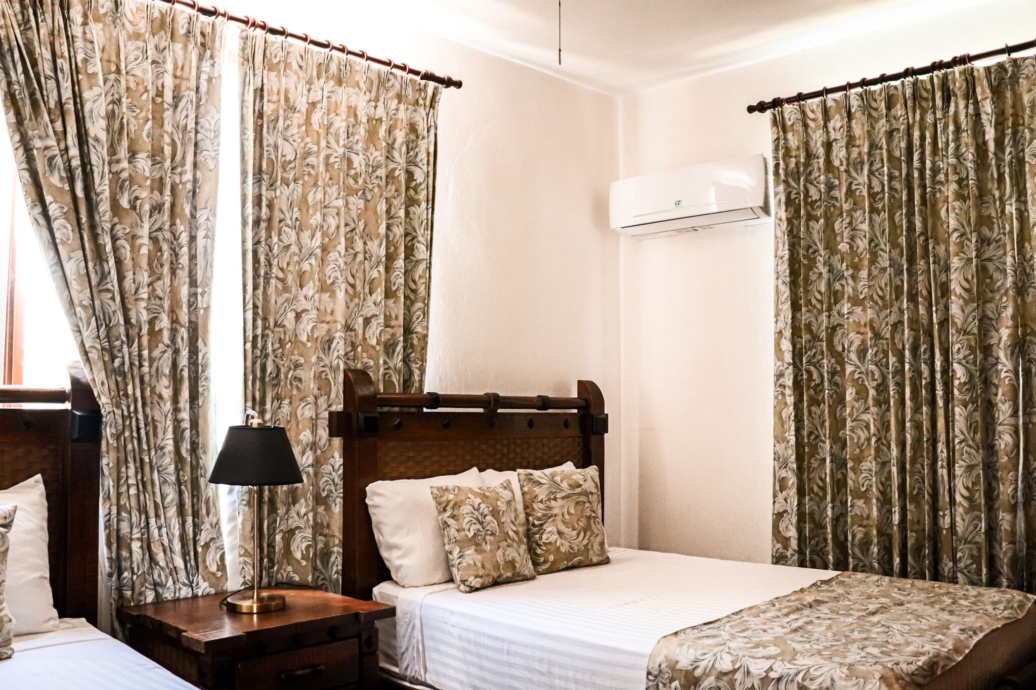 A hotel room with a bed, a nightstand, a lamp, and floral curtains.