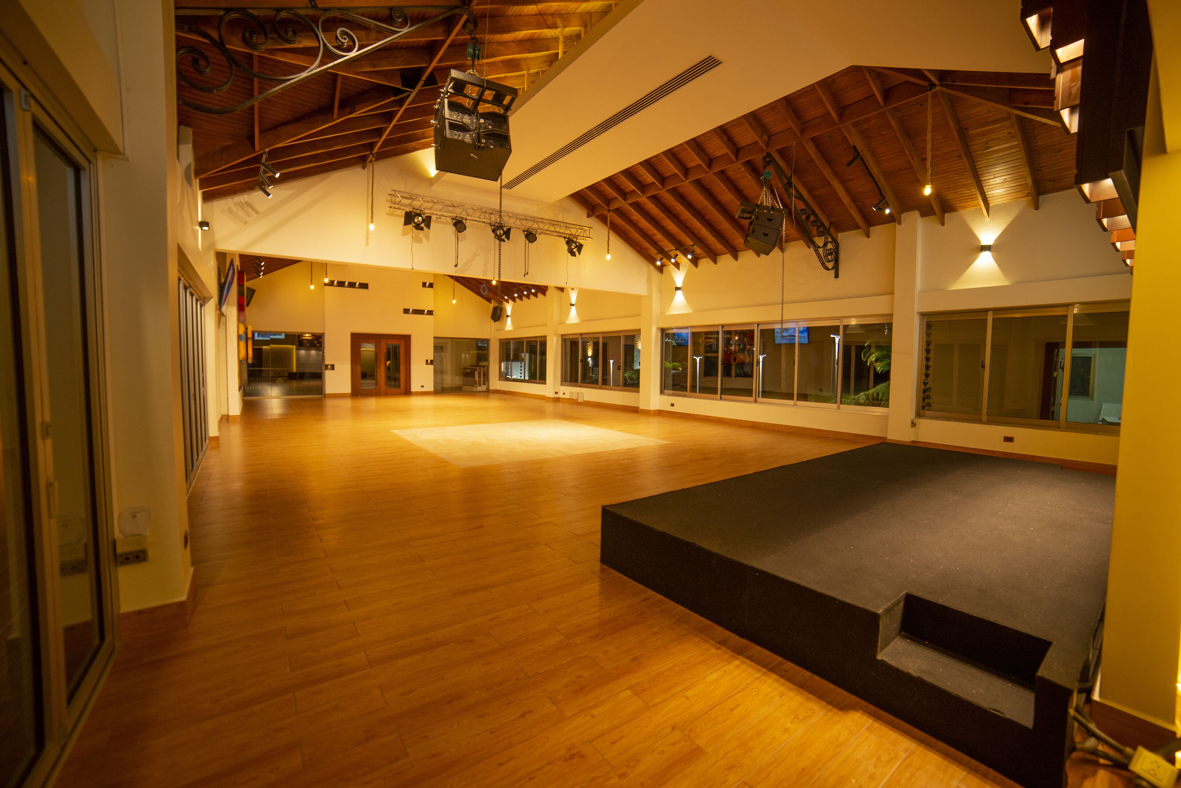 Un espacio interior amplio con suelo de madera, ventanas grandes y un escenario.