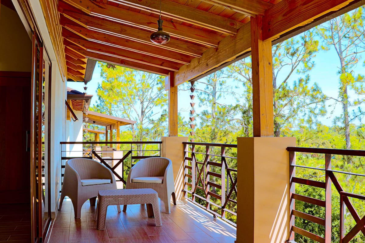 A wooden deck with wicker furniture, a view of trees, and a clear sky.