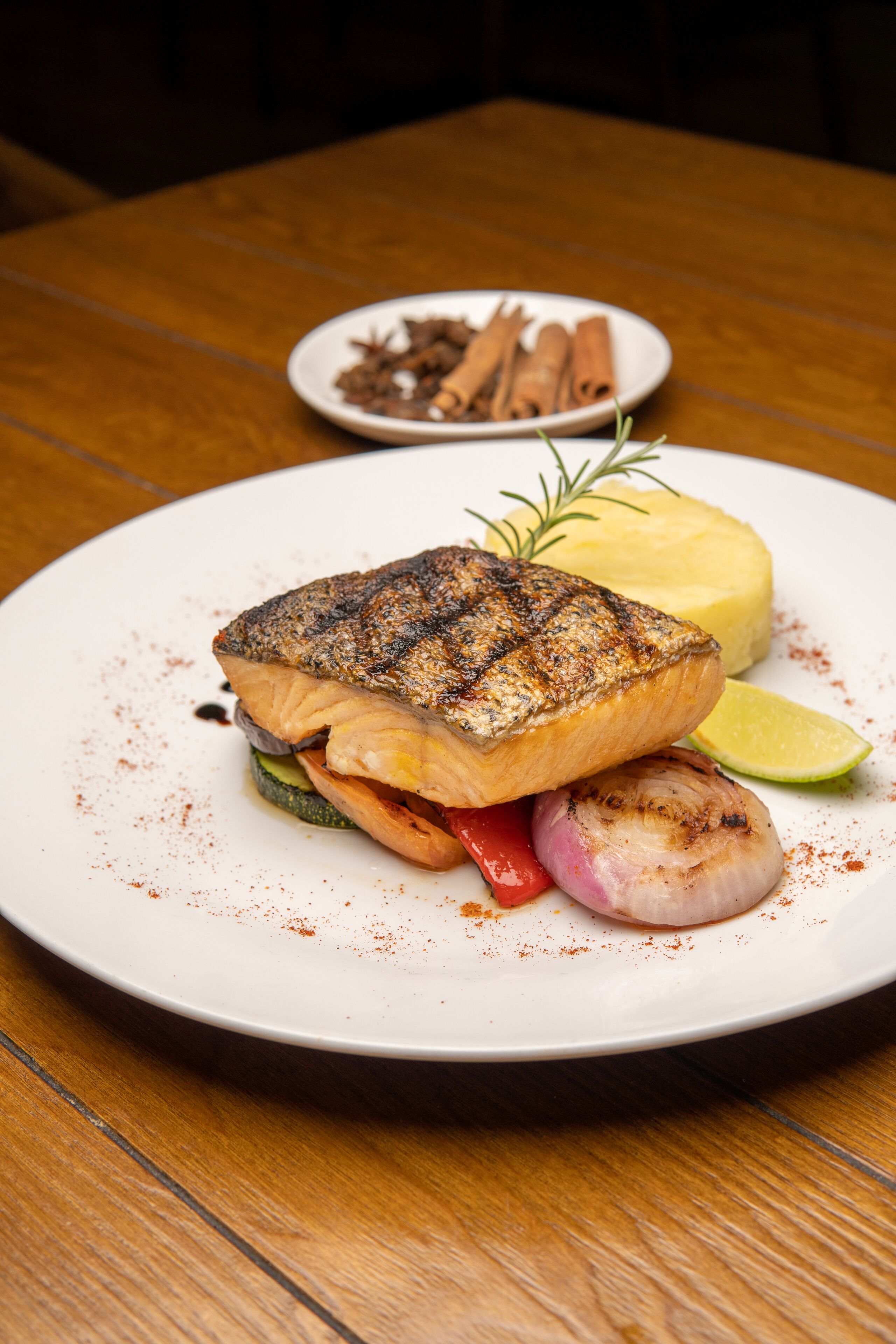 En tallrik med grillad fisk, grönsaker och en skiva citron, serverat på en vit tallrik.