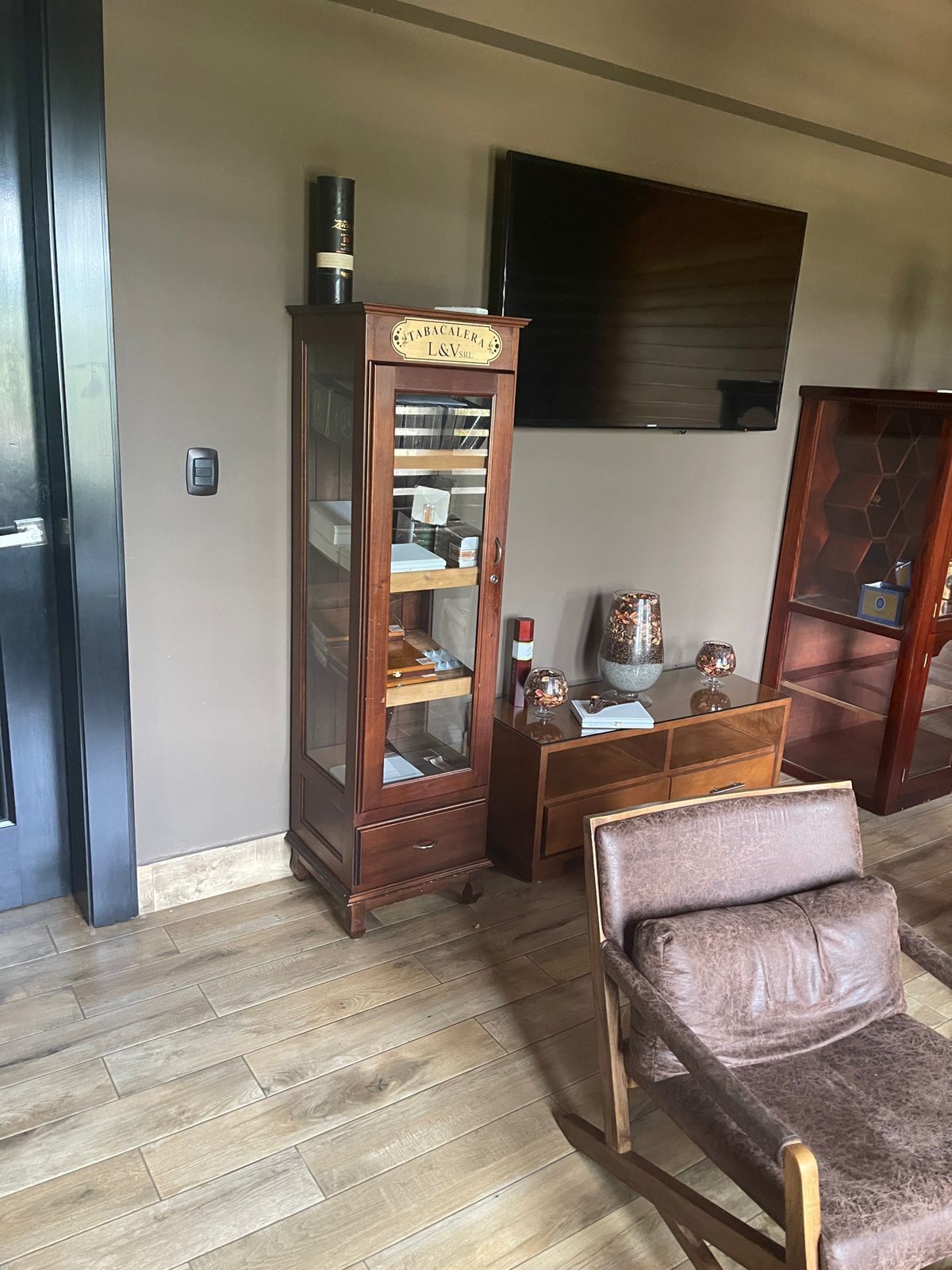 Una habitación con un armario de madera, un televisor montado en la pared y un sillón de cuero.