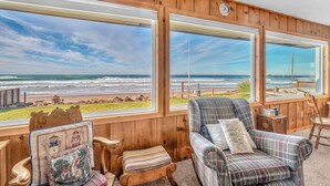 Una habitación con grandes ventanales que dan a una playa, paredes de madera y dos sillones a cuadros.