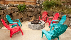 Ein Feuerkorb, umgeben von bunten Adirondack-Stühlen in einem Garten.