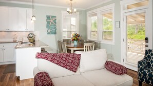 Eine moderne Küche mit weißen Schränken, ein Essbereich mit Tisch und Stühlen sowie eine gemütliche Sitzecke mit einer Couch und gemusterten Kissen.