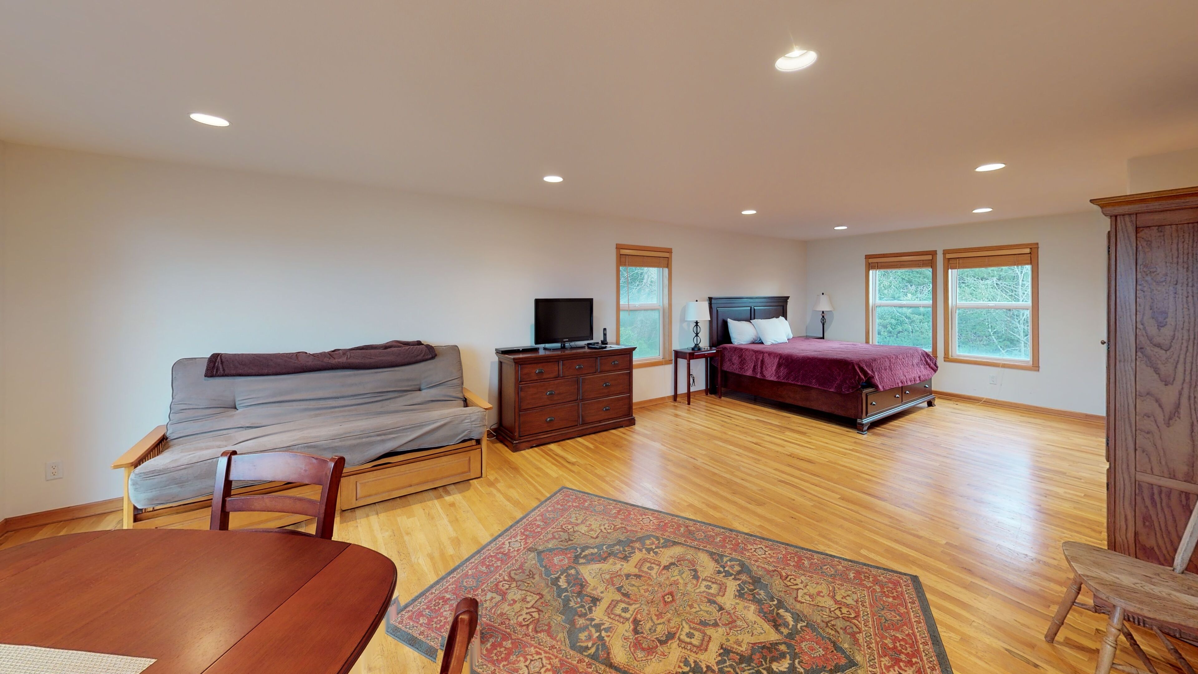 A bedroom with a sofa, a bed, a dresser, a TV, and a rug.