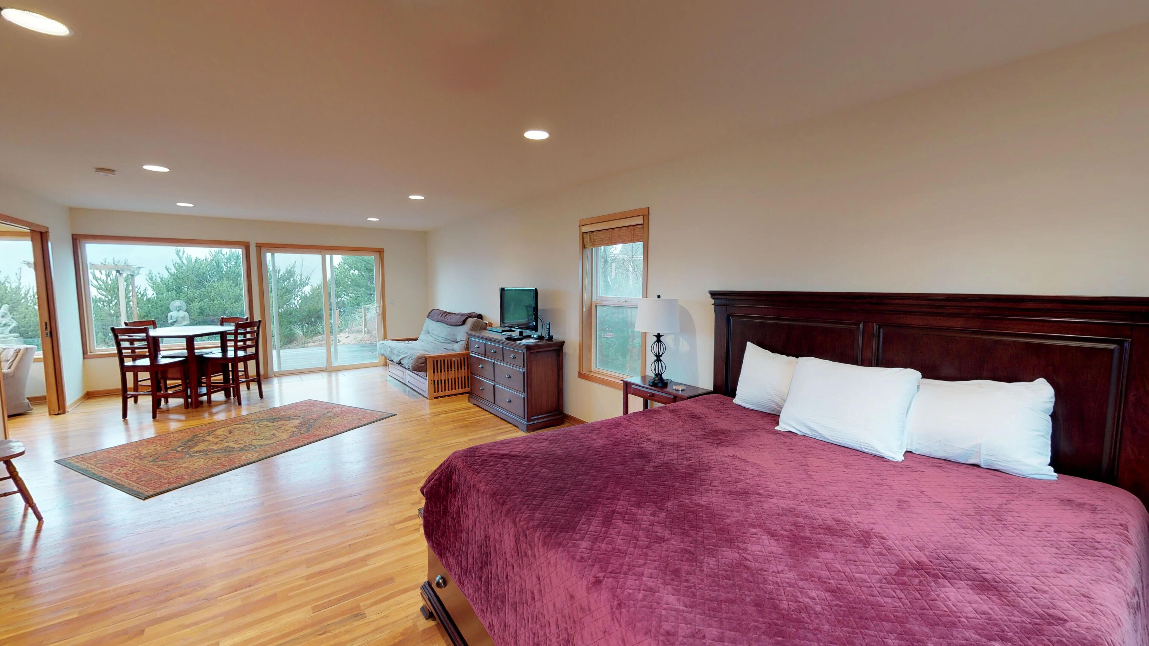 A spacious bedroom with a large bed, a desk, and a chair, a dresser, and a TV.