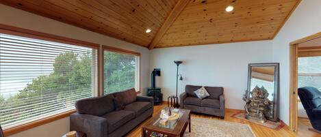 A spacious living room with a wooden ceiling, large windows, a sofa, a coffee table, and a fireplace.