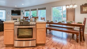 A modern kitchen with a built-in oven, a dining table with benches, and large windows offering a view of the outdoors. - The perfect beach home for 10, 3 blocks to the beach, ocean views from the deck. (Lincoln City)