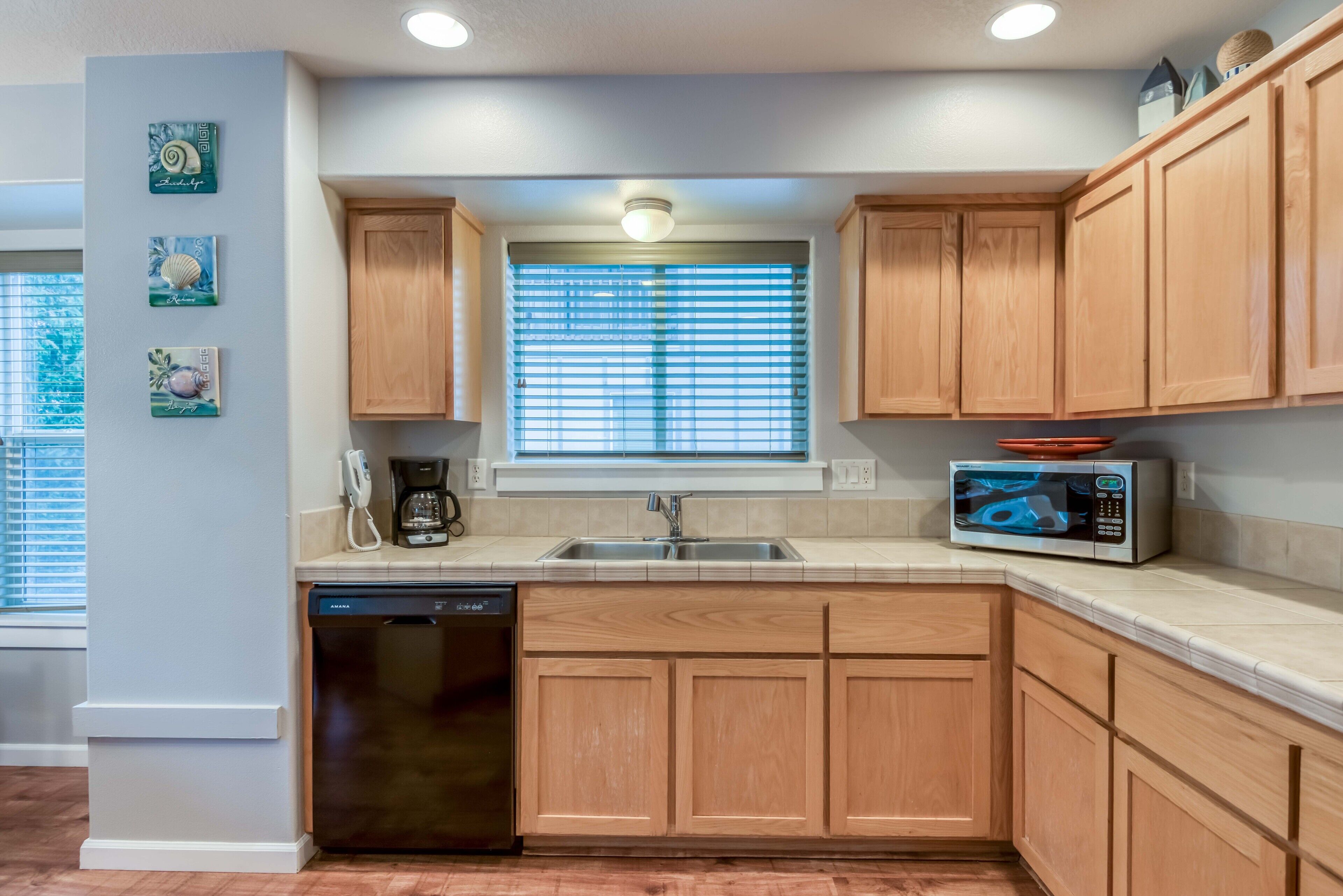 A kitchen with wooden cabinets, a dishwasher, a microwave, and a window with blinds.