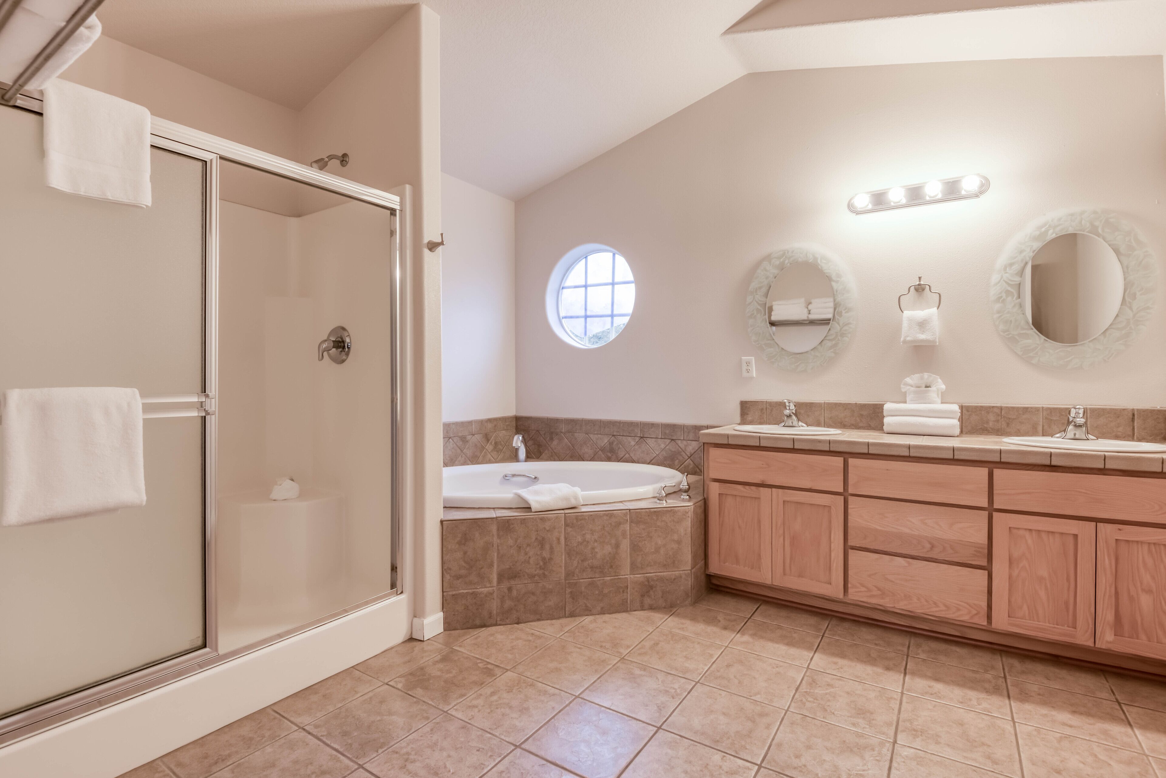 A modern bathroom with a glass shower enclosure, a freestanding bathtub, and a vanity with a mirror and lights.