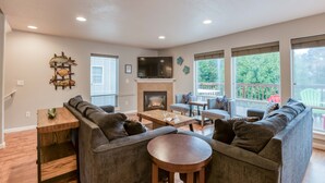 A spacious living room with a fireplace, large windows, and a balcony. - The perfect beach home for 10, 3 blocks to the beach, ocean views from the deck. (Lincoln City)
