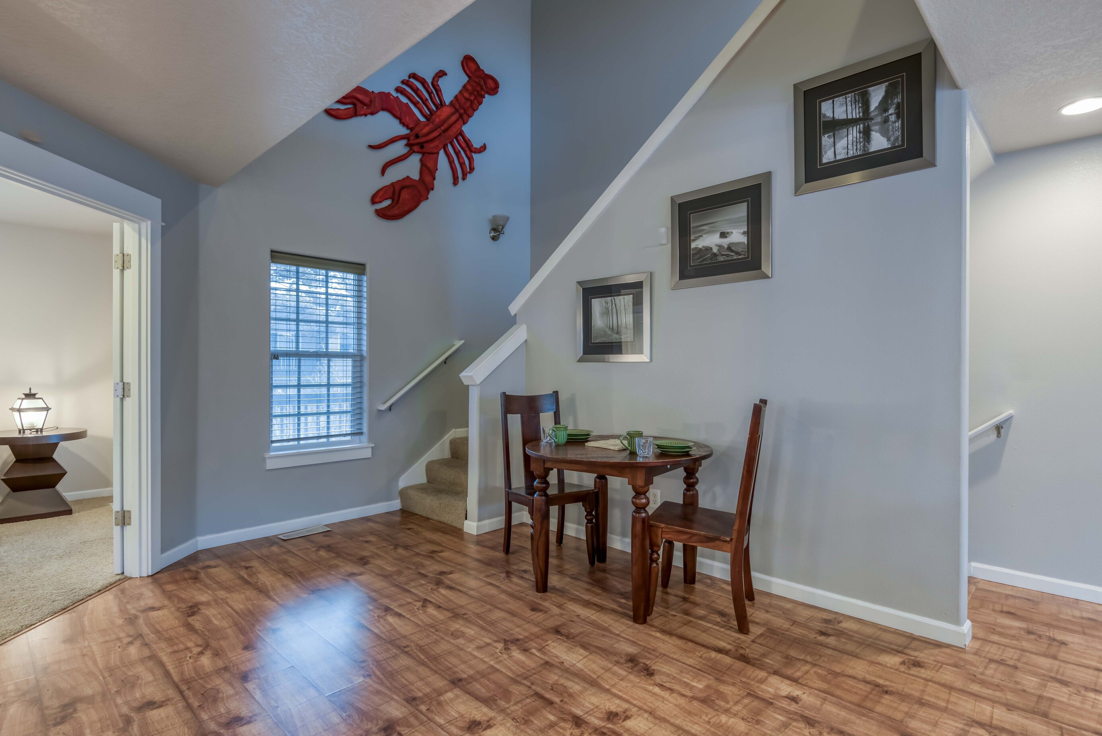 Un coin repas avec une table et des chaises en bois, une décoration murale représentant un crabe rouge et un escalier.