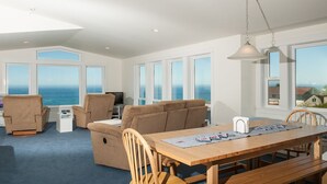 Ett rymligt vardagsrum med ett stort fönster med utsikt över havet, ett matbord i trä och bekväma sittplatser.
